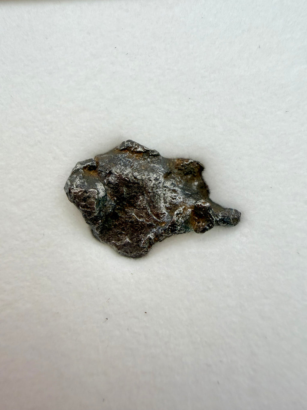 Gebel Kamil ataxite meteorite 1.00g -- smooth metallic exterior showing impact fragmentation surfaces and iron luster