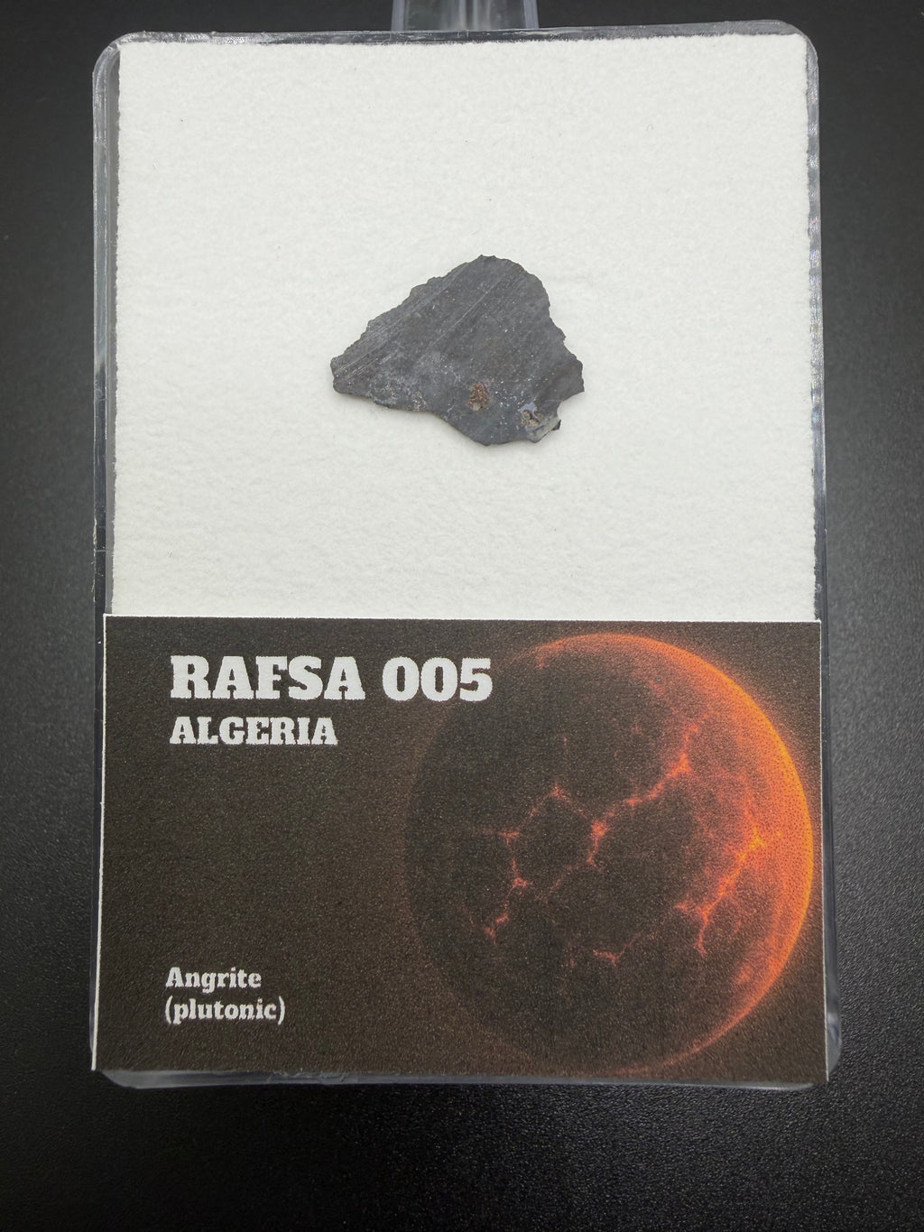 meteorite sample in a display case with 'RAFSA 005 Algeria' label on a dark background