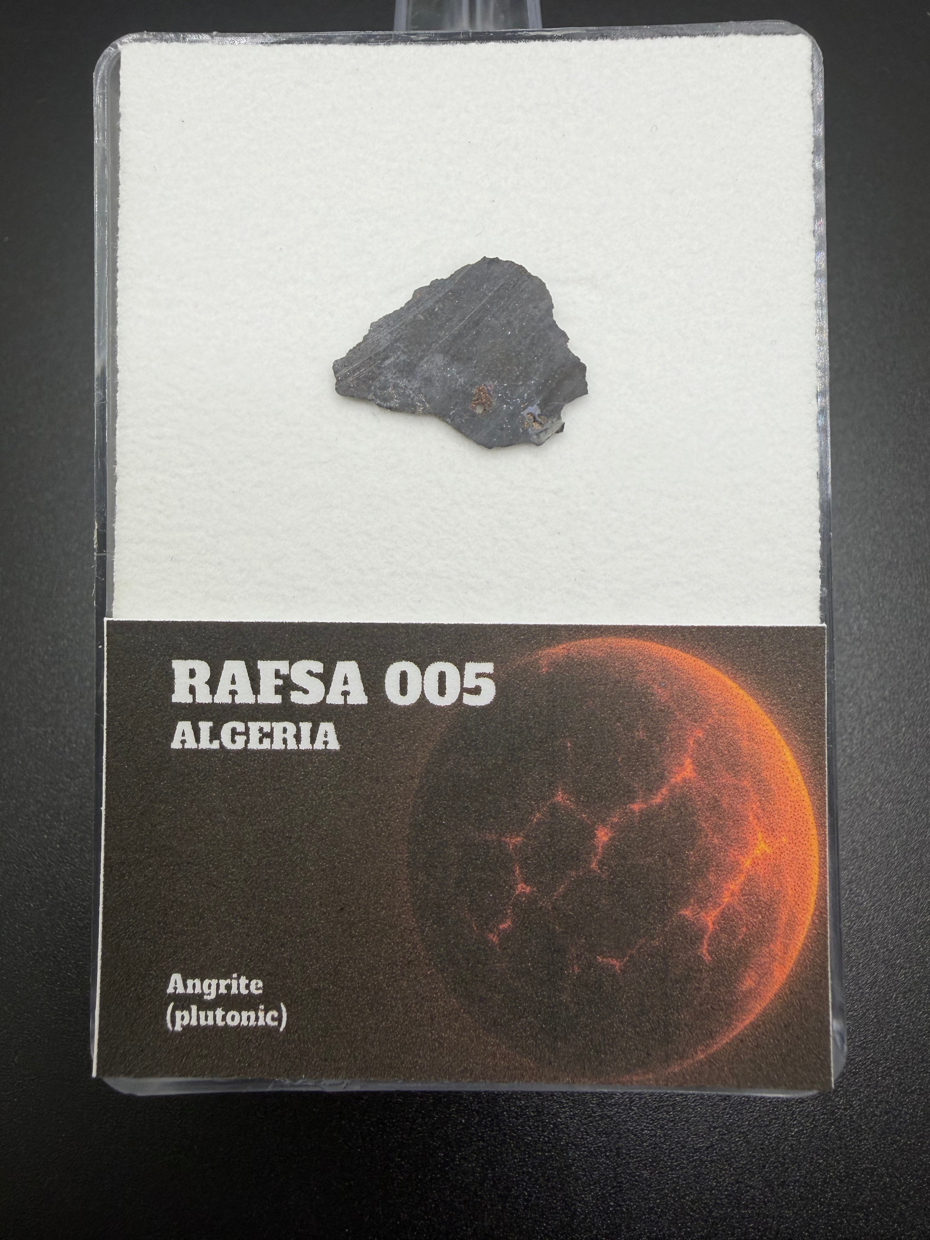 meteorite sample in a display case with 'RAFSA 005 Algeria' label on a dark background