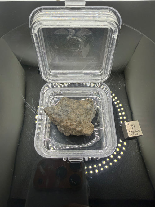 Adrar 013 lunar meteorite 14.76g in display case showing flow banded melt matrix with high relief mineral clasts