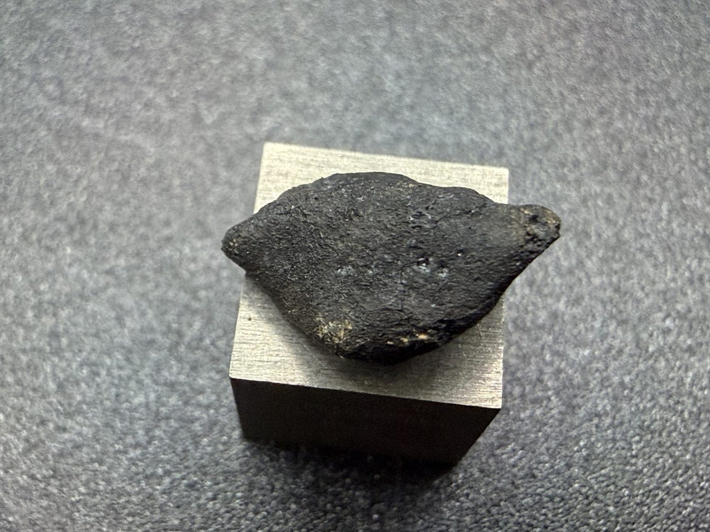 Ait Saoun EH3 enstatite chondrite, 0.67g individual, black fusion crust, profile view on a 1 cm cube