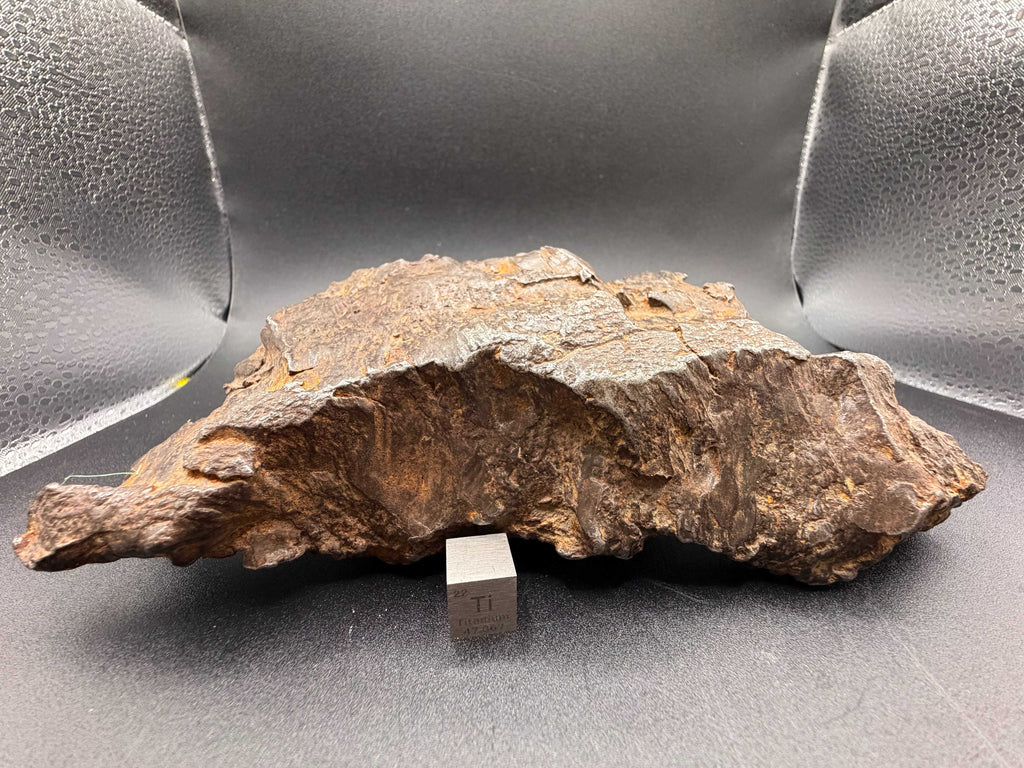 Gebel Kamil 1414g iron meteorite displayed with a titanium scale cube, showing the broad sheared face