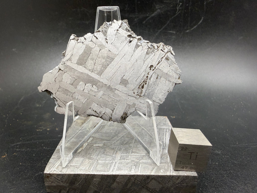 Kaalijärv iron meteorite 31.18g full slice on acrylic display stand front view showing broad kamacite banding and Widmanstätten pattern with titanium cube for scale