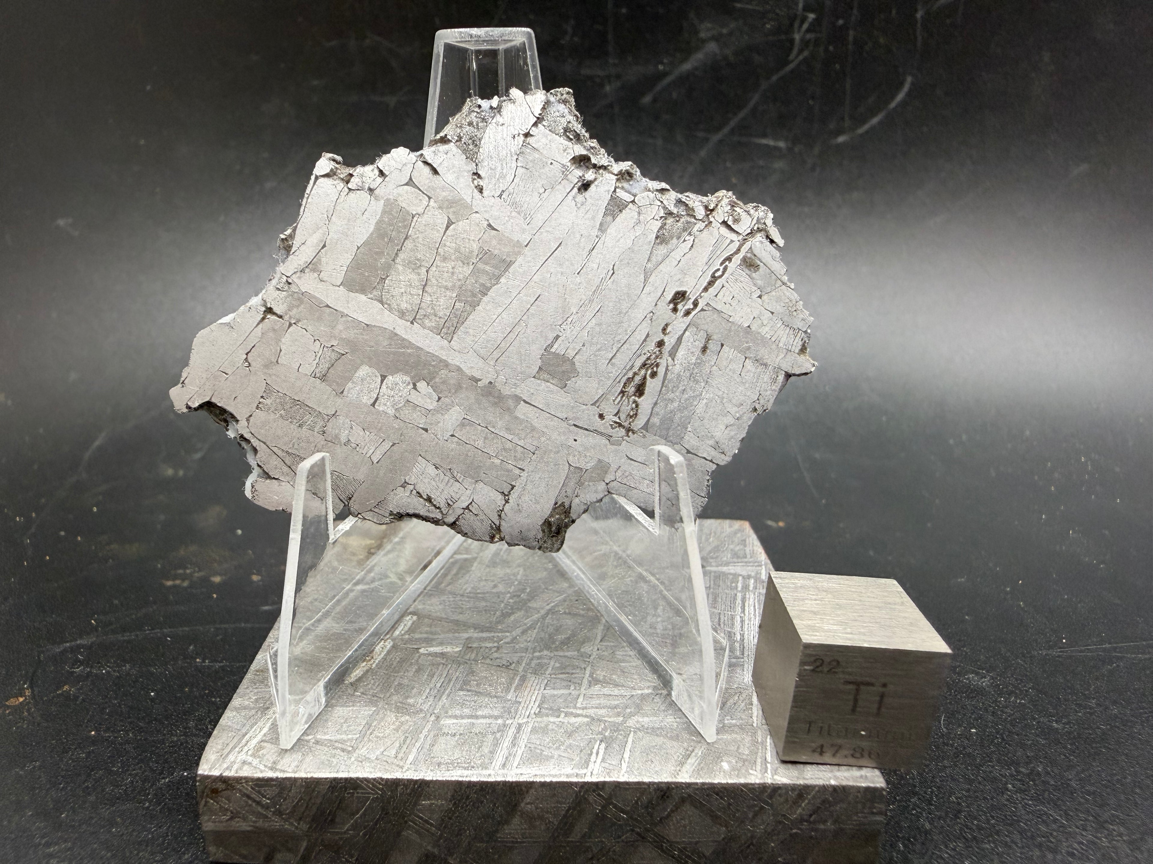 Kaalijärv iron meteorite 31.18g full slice on acrylic display stand front view showing broad kamacite banding and Widmanstätten pattern with titanium cube for scale