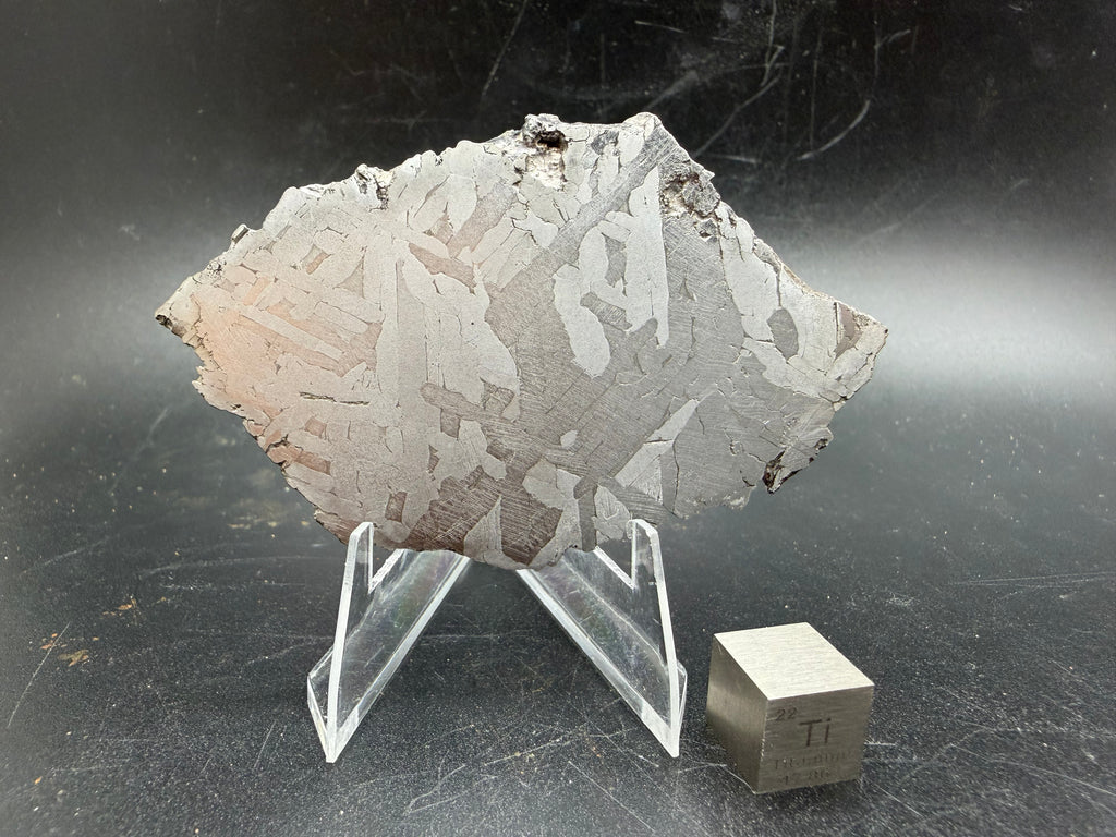 Kaalijärv iron meteorite 45.71g full slice on acrylic display stand front view showing Widmanstätten pattern with titanium cube for scale