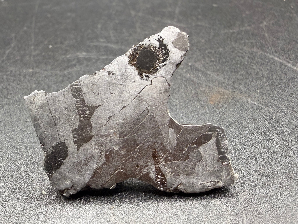 Kaalijarv iron meteorite, IAB-MG, 12.82 g slice standing upright, full etched face with lighter kamacite areas, darker zones crossed by Neumann bands, and a dark rounded nodule near the top