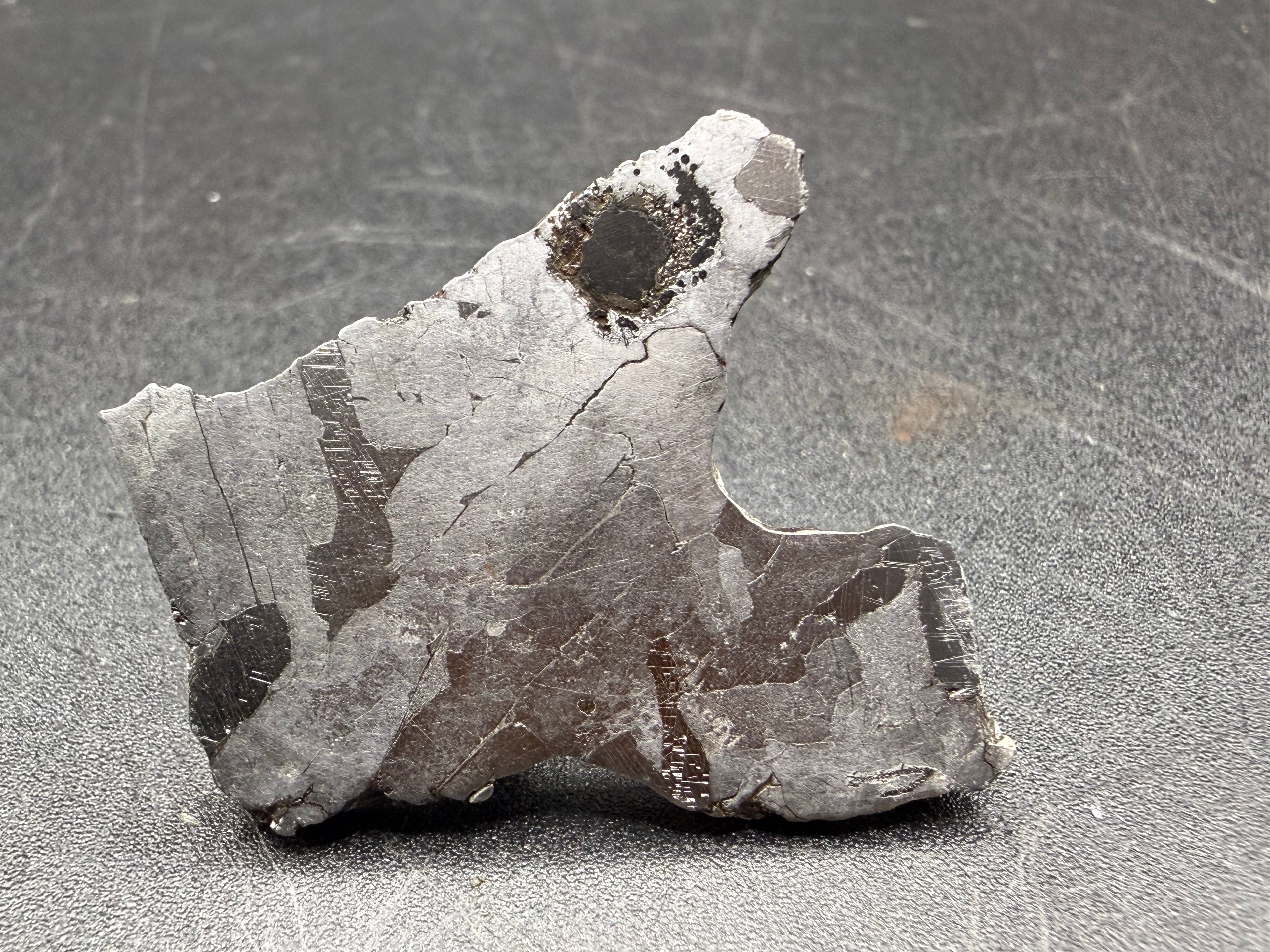 Kaalijarv iron meteorite, IAB-MG, 12.82 g slice standing upright, full etched face with lighter kamacite areas, darker zones crossed by Neumann bands, and a dark rounded nodule near the top
