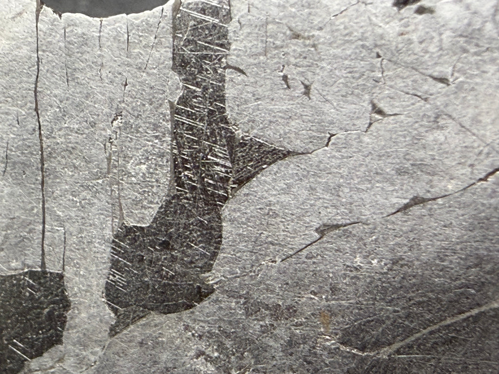 Kaalijarv iron meteorite, IAB-MG, 12.82 g slice, close-up of the etched face with darker zones crossed by fine Neumann bands between lighter kamacite areas