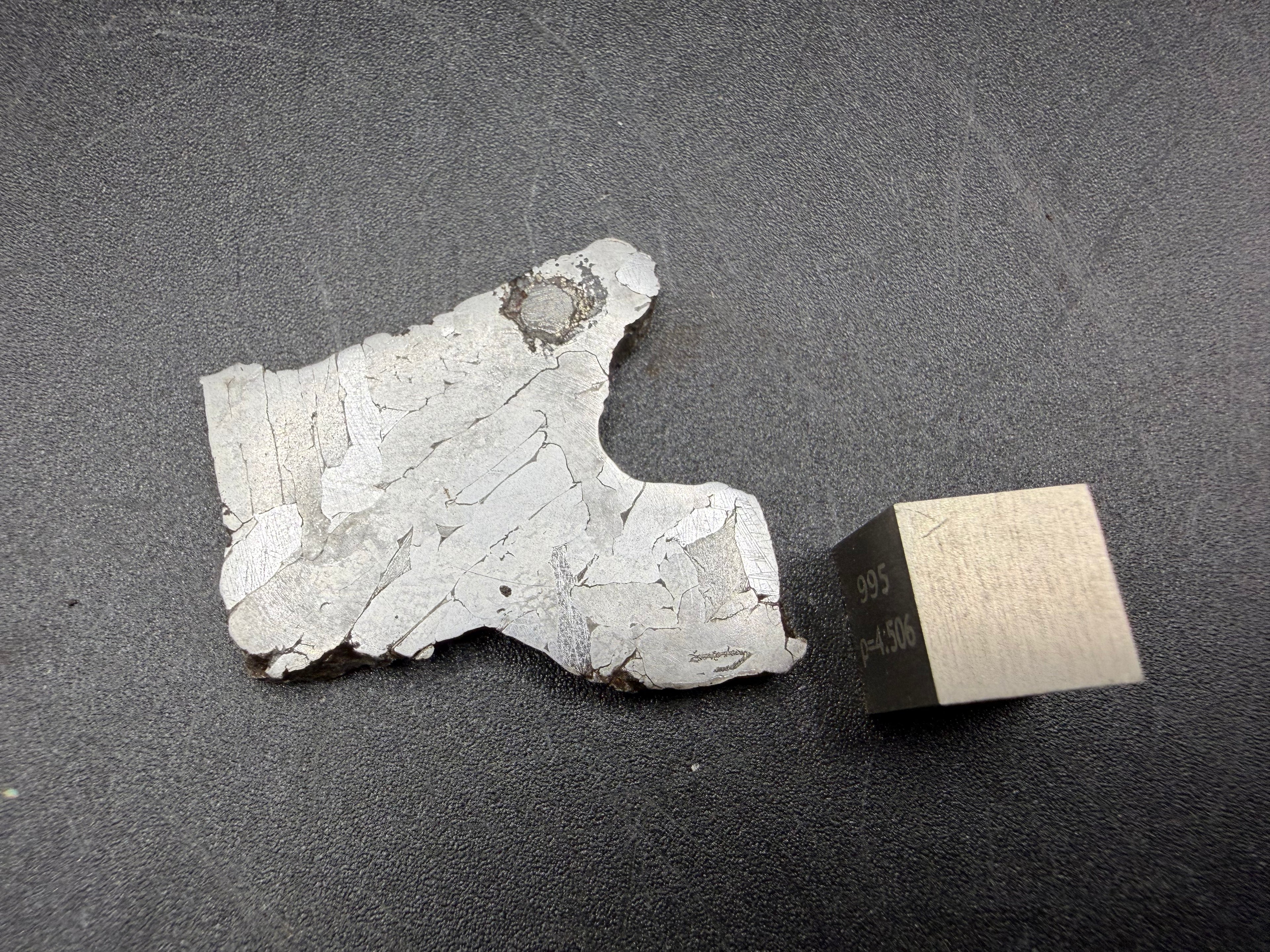 Kaalijarv iron meteorite, IAB-MG, 12.82 g slice lying flat, reverse face with lighter kamacite plates and the dark nodule visible at the upper edge