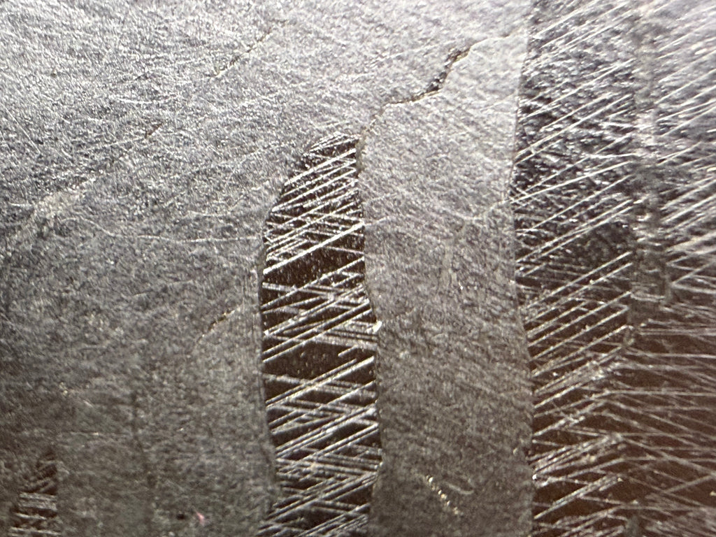 Kaalijarv iron meteorite, IAB-MG, 127.37 g end cut, close-up of the etched cut face showing intersecting sets of fine straight Neumann bands in the darker zones between lighter, smoother zones