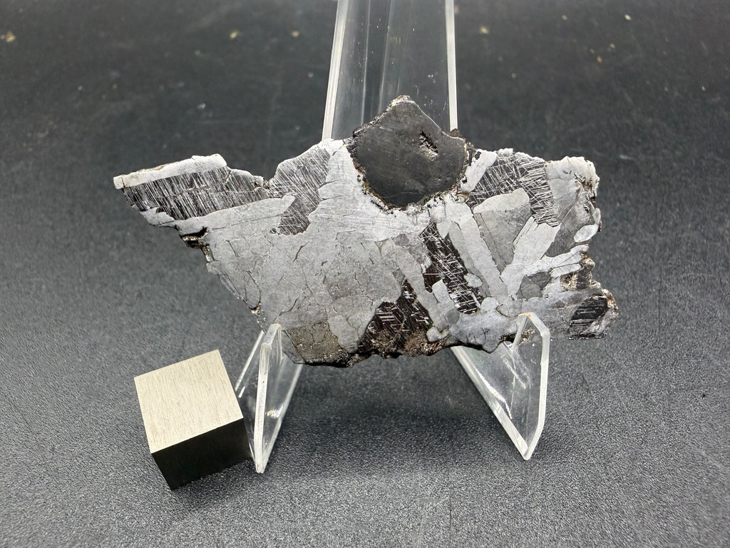 Kaalijarv iron meteorite, IAB-MG, 15.78 g etched slice standing upright, with a rounded dark inclusion at the top edge and Neumann bands across the darker metal