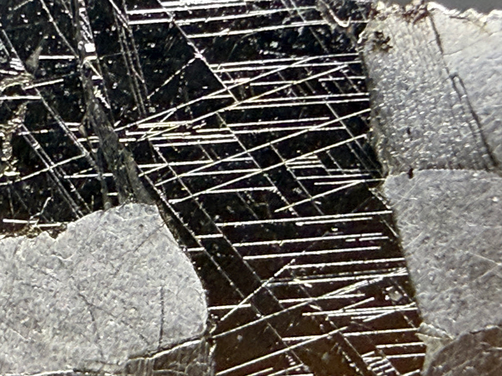 Kaalijarv iron meteorite, IAB-MG, 15.78 g slice, close-up of the etched face showing dense intersecting Neumann bands in a dark zone bordered by lighter, smoother metal