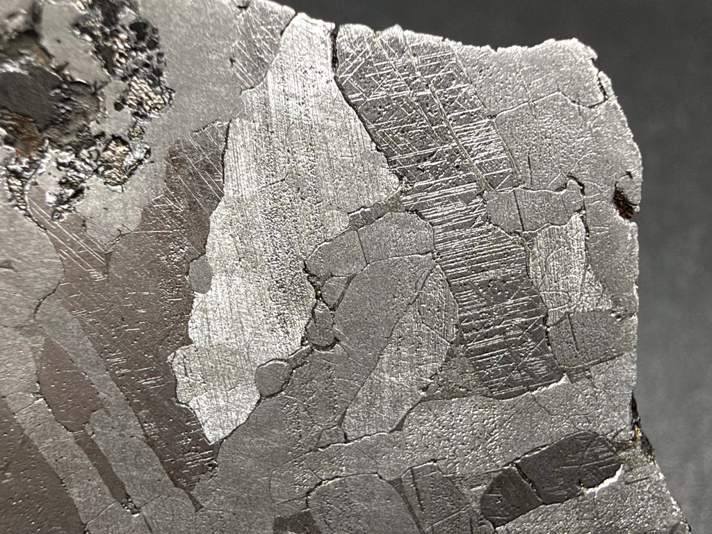 Kaalijarv IAB-MG iron meteorite slice, 17.00 g, close-up of the reverse face with Neumann bands crossing kamacite crystals and the edge of the dark inclusion at upper left