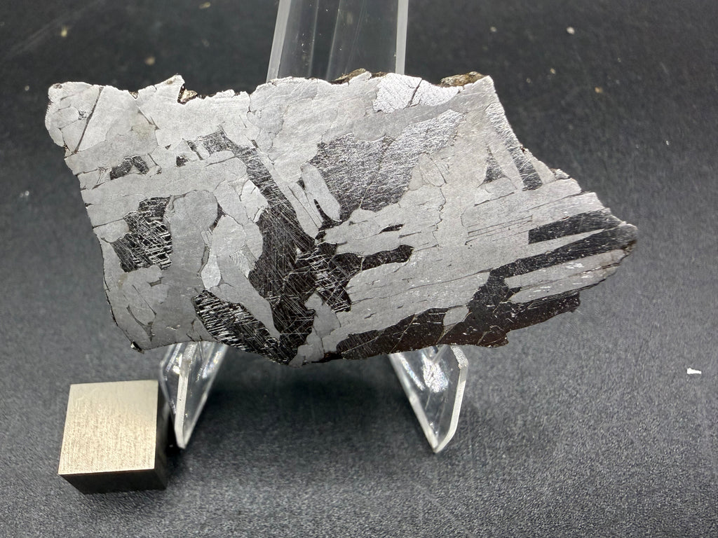 Kaalijarv iron meteorite, IAB-MG, 21.00 g slice on a clear acrylic stand with a scale cube, full view of the etched face showing high-contrast bright and dark Widmanstatten plates, with fine Neumann bands in the dark plates