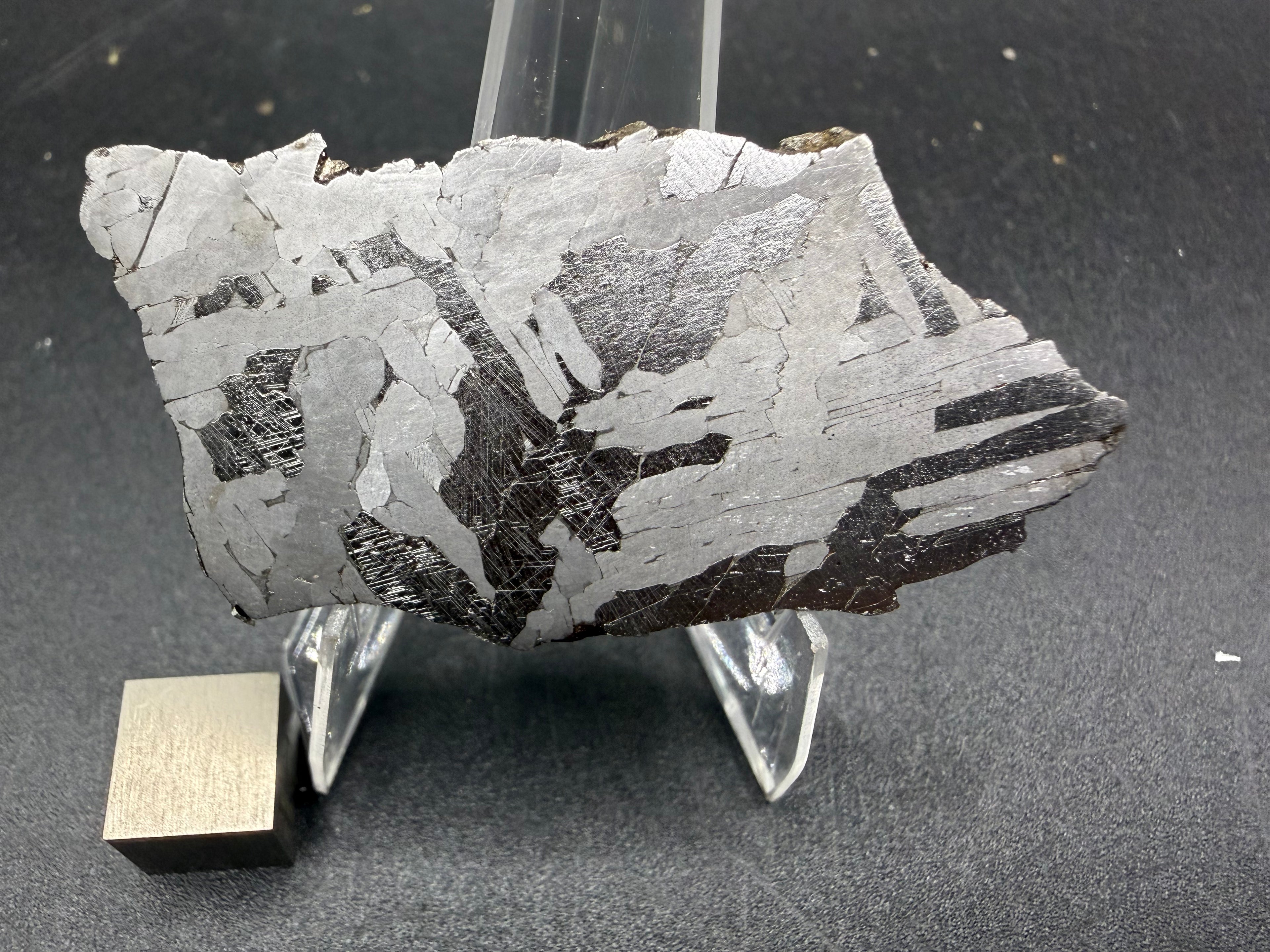 Kaalijarv iron meteorite, IAB-MG, 21.00 g slice on a clear acrylic stand with a scale cube, full view of the etched face showing high-contrast bright and dark Widmanstatten plates, with fine Neumann bands in the dark plates