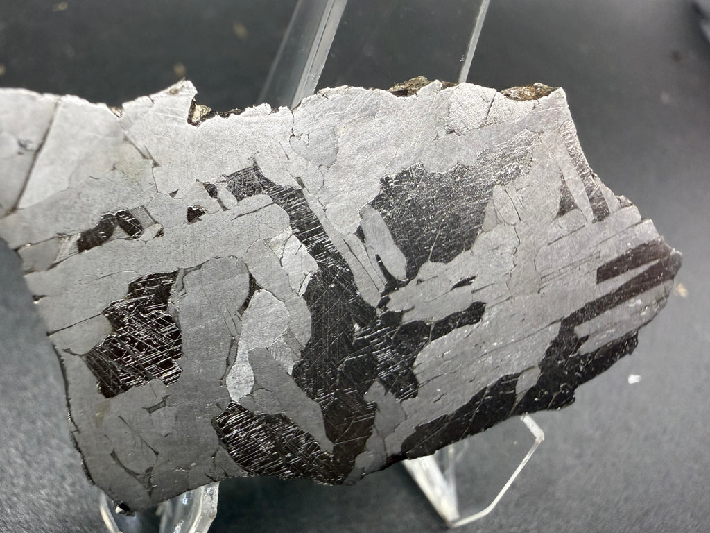 Kaalijarv iron meteorite, IAB-MG, 21.00 g slice on a clear acrylic stand, closer view of the left side of the etched face showing dark plates with Neumann bands between bright and gray plates