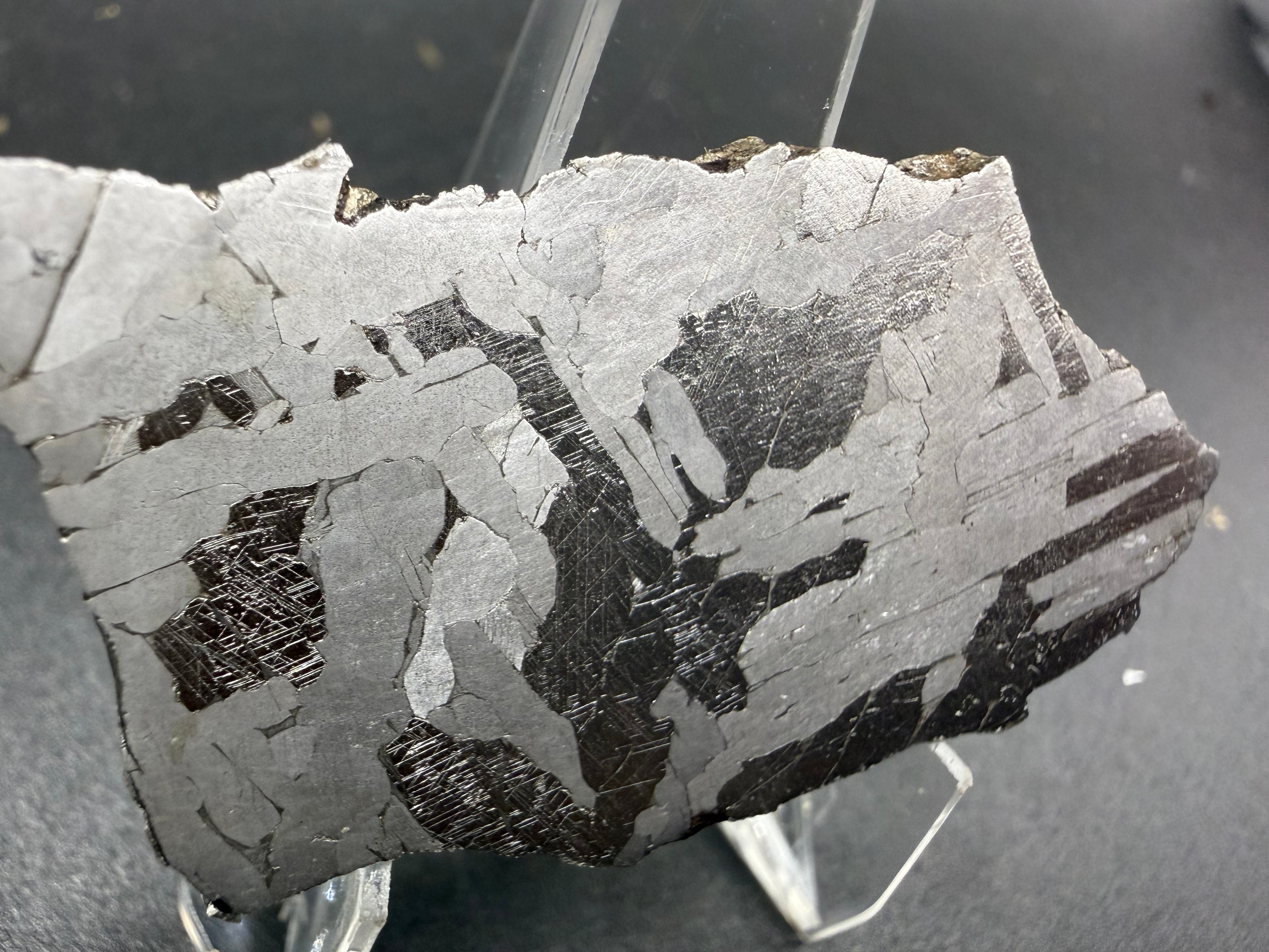 Kaalijarv iron meteorite, IAB-MG, 21.00 g slice on a clear acrylic stand, closer view of the left side of the etched face showing dark plates with Neumann bands between bright and gray plates