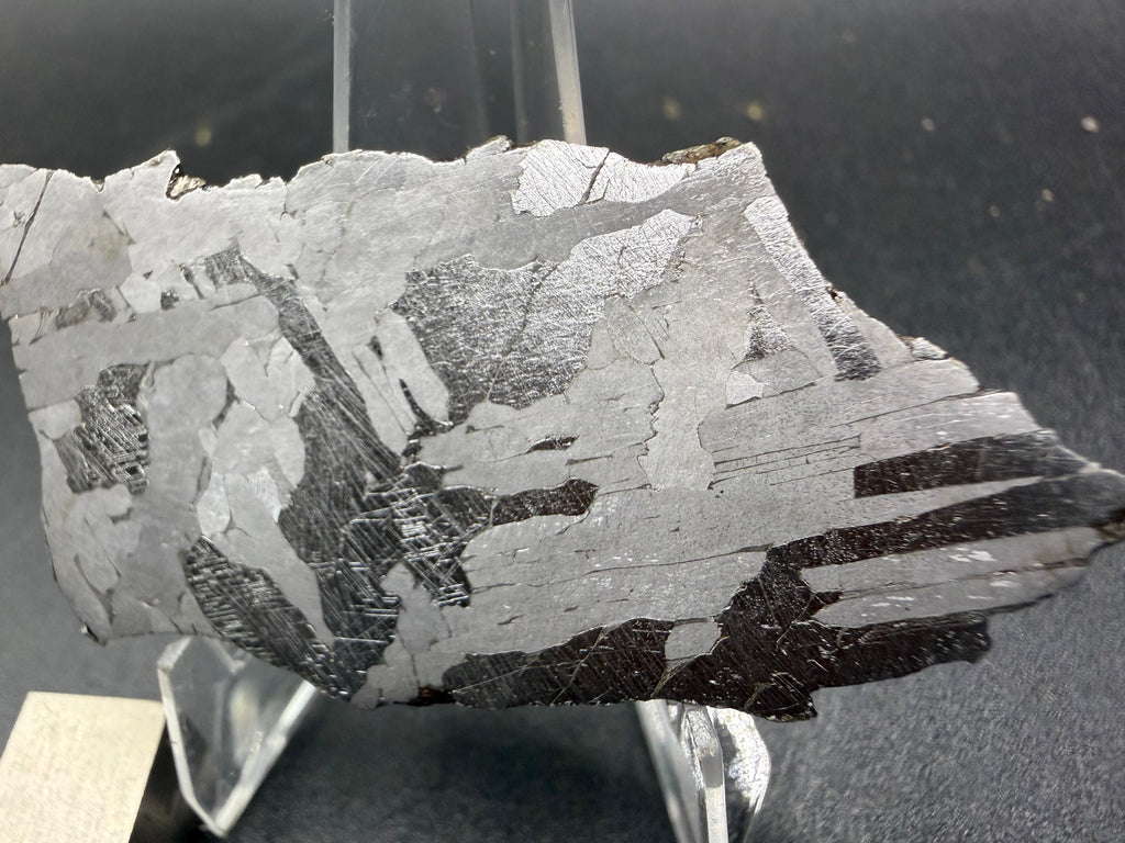 Kaalijarv iron meteorite, IAB-MG, 21.00 g slice on a clear acrylic stand, closer view of the right side of the etched face showing dark plates with Neumann bands between bright and gray plates
