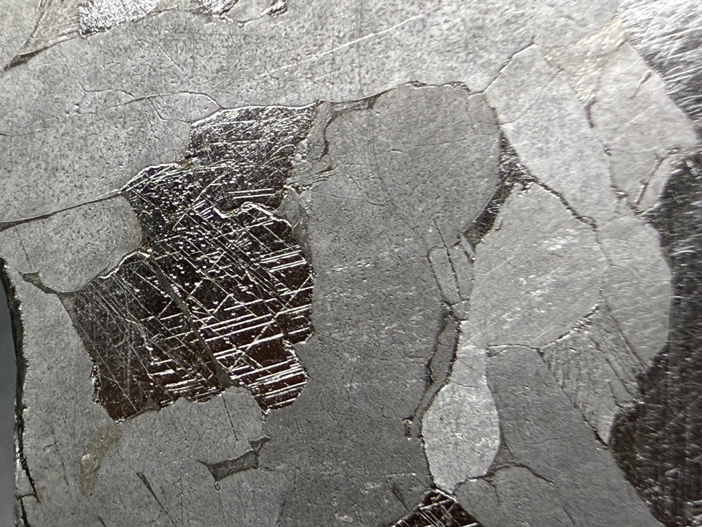 Kaalijarv iron meteorite, IAB-MG, 21.00 g slice, close-up of a dark plate on the etched face crossed by several intersecting sets of fine straight Neumann bands