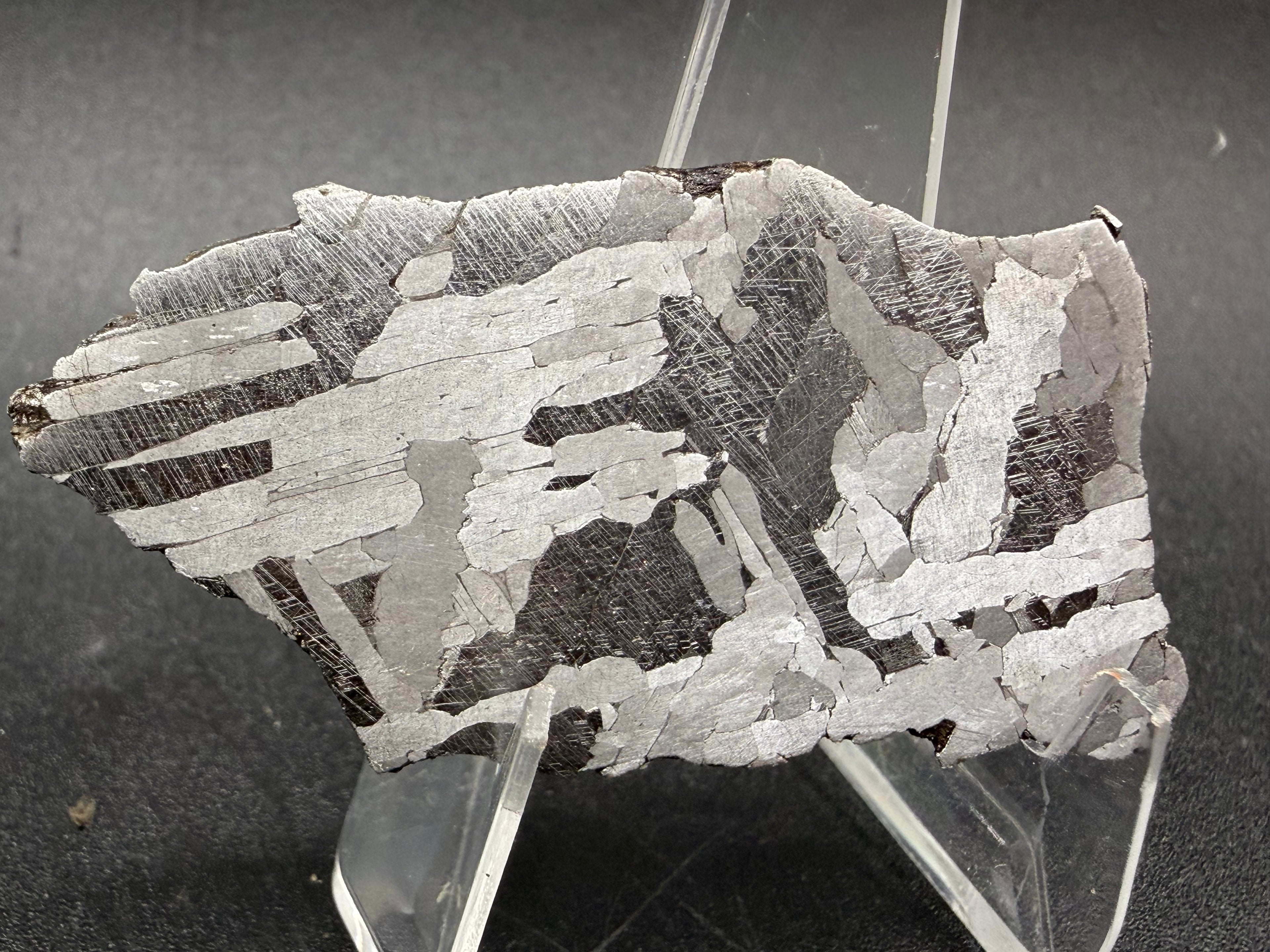 Kaalijarv iron meteorite, IAB-MG, 21.00 g slice on a clear acrylic stand, etched face at an angle showing bright and dark crossing Widmanstatten plates, with fine Neumann bands in the darker plates