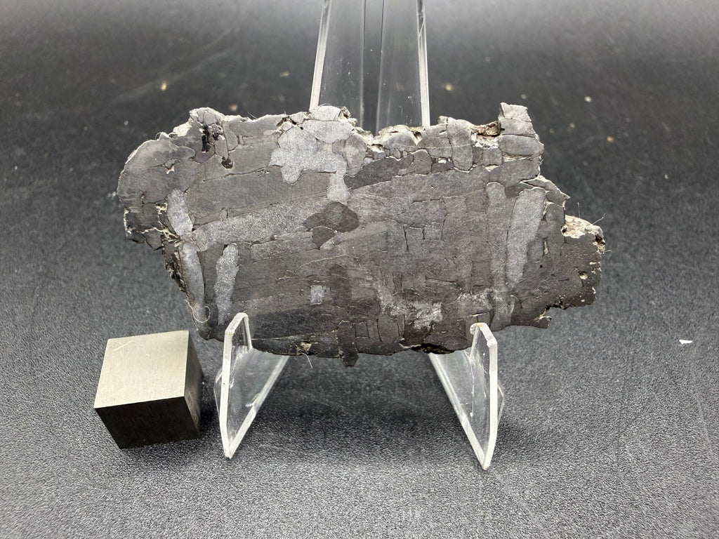 Kaalijarv iron meteorite, IAB-MG, 21.42 g slice on a clear acrylic stand with a scale cube, full view of the etched face showing the Widmanstatten pattern and weathered edges