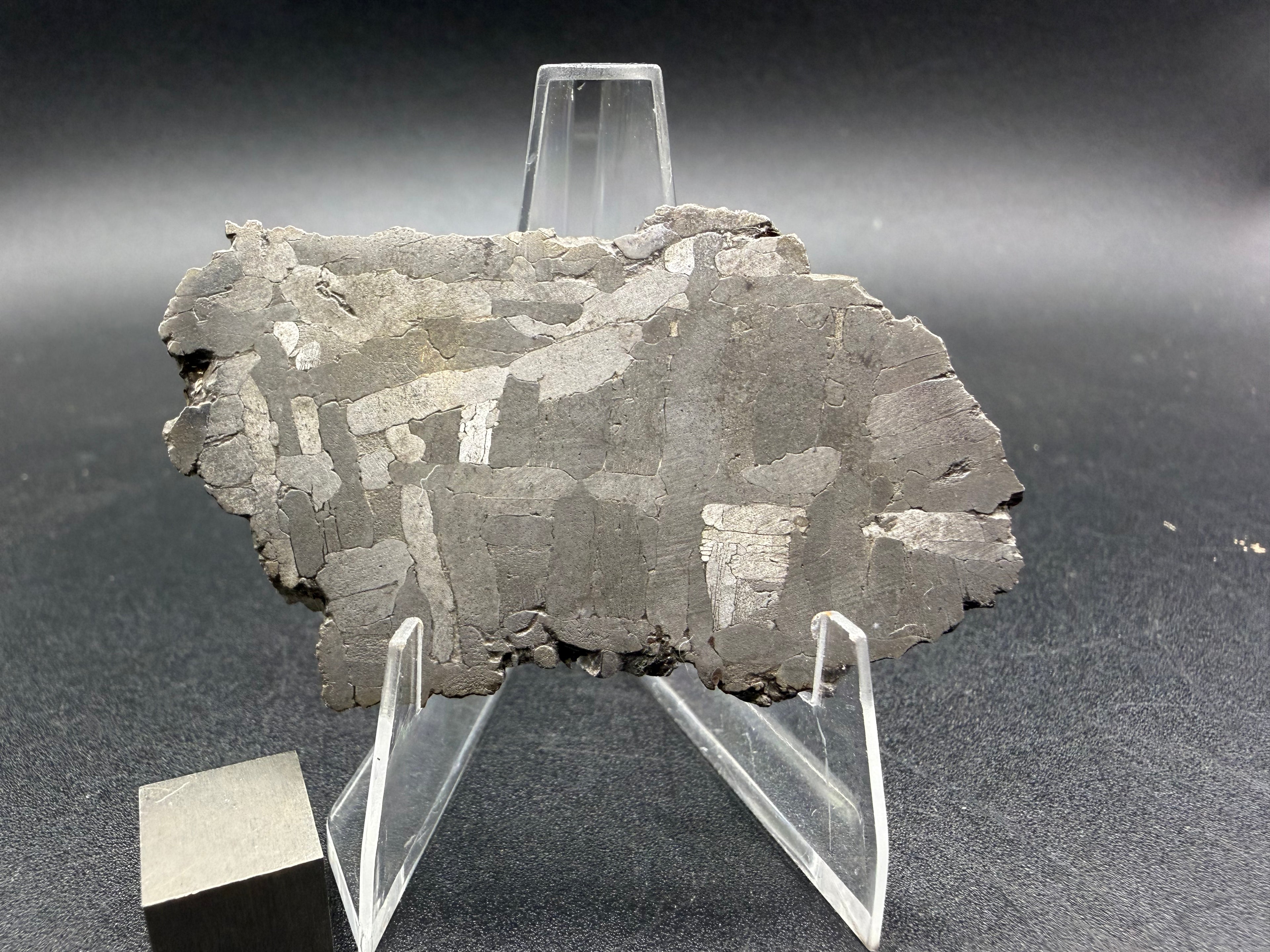 Kaalijarv iron meteorite, IAB-MG, 28.43 g slice standing upright, etched face under bright light with gray kamacite plates and scattered bright plates
