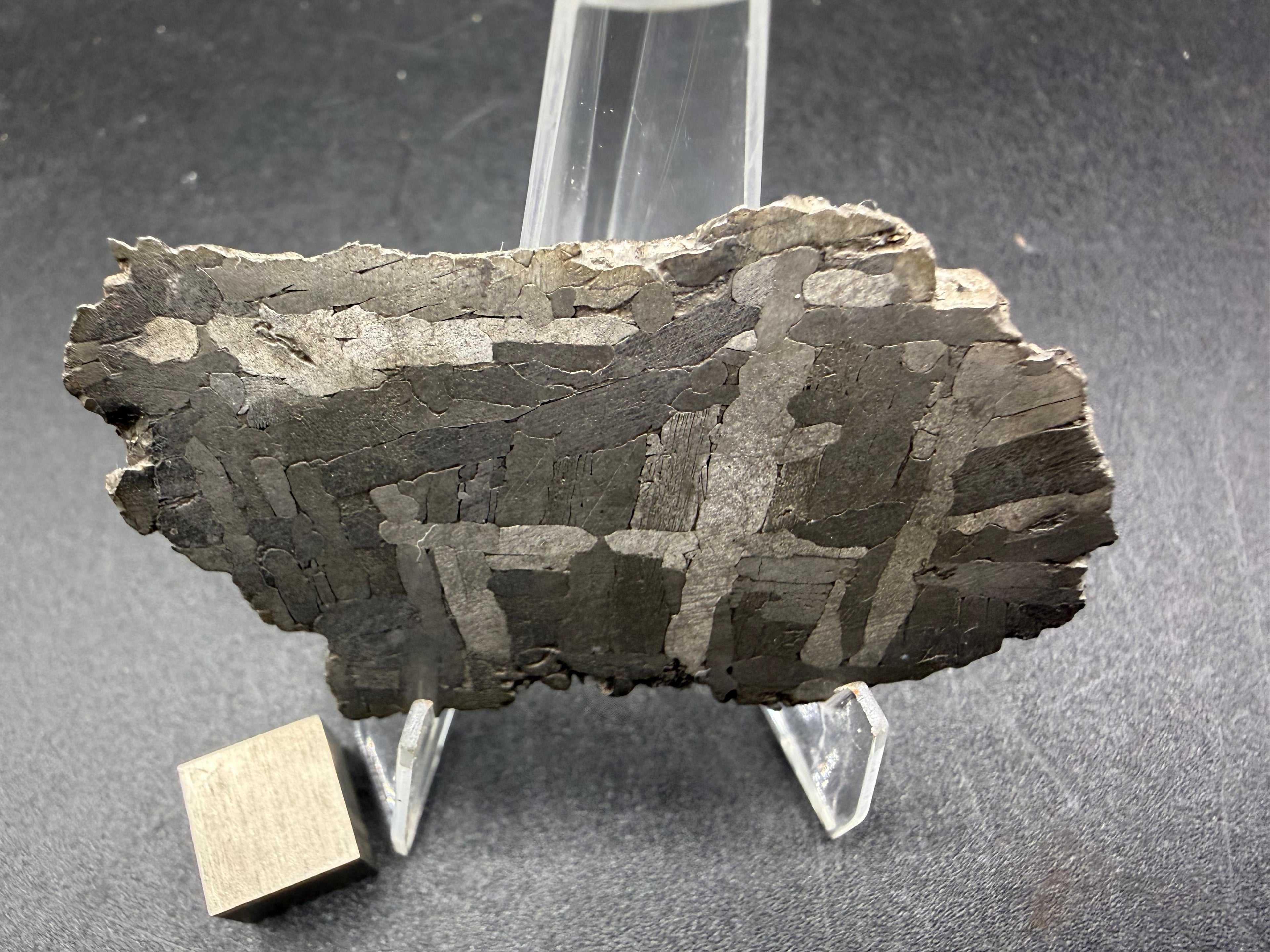 Kaalijarv iron meteorite, IAB-MG, 28.43 g slice standing upright, etched face in low light with gray kamacite plates crossing over darker areas