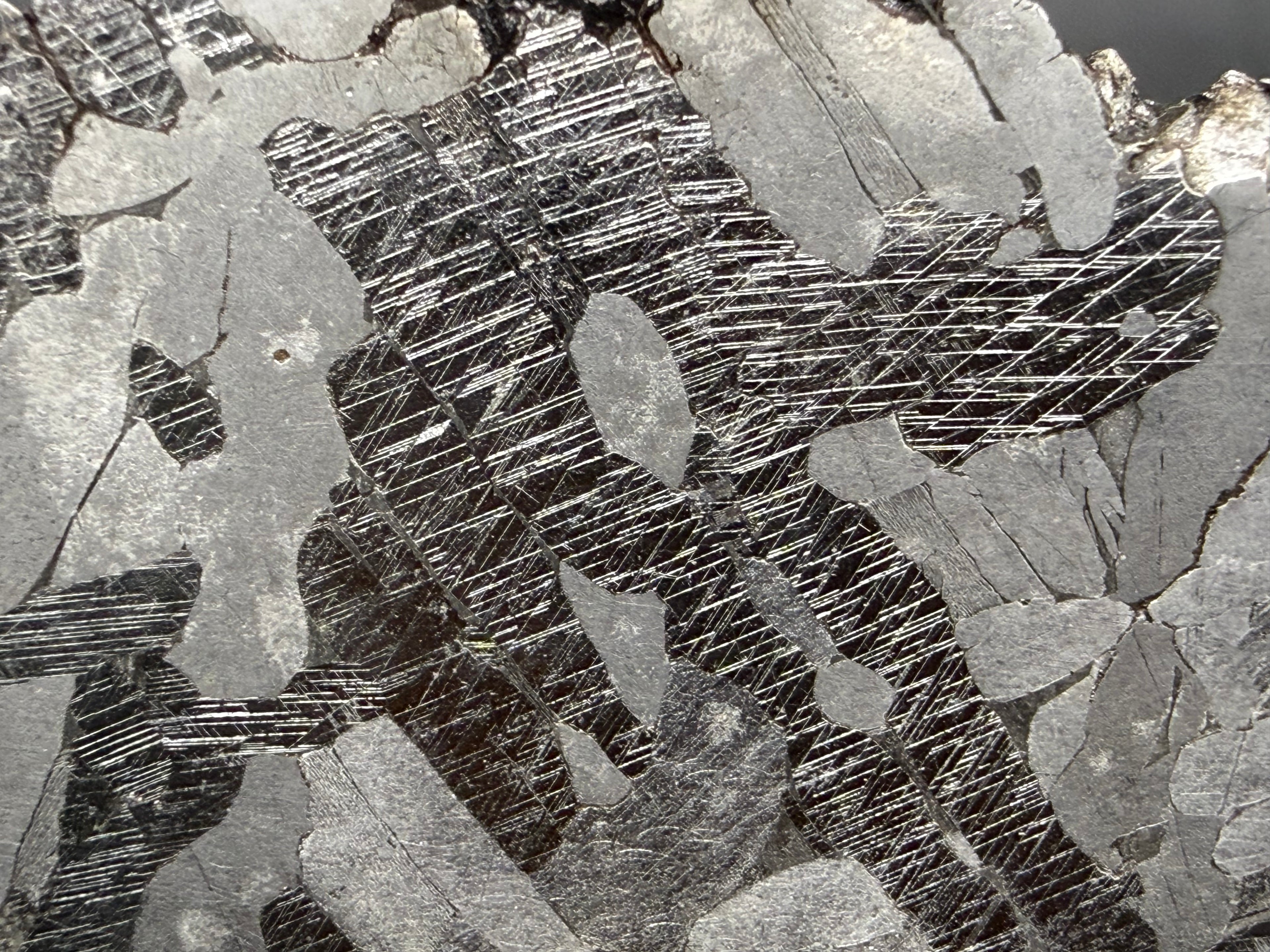 Kaalijarv iron meteorite, IAB-MG, 33.88 g slice, close-up of the etched face showing several intersecting sets of Neumann bands crossing the darker zones