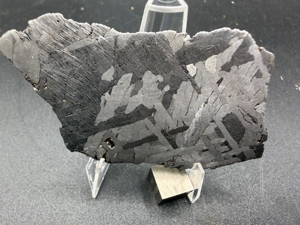 Kaalijarv iron meteorite, IAB-MG, 39.28 g slice standing upright, etched face in low light with lighter kamacite plates crossing at angles against a dark background