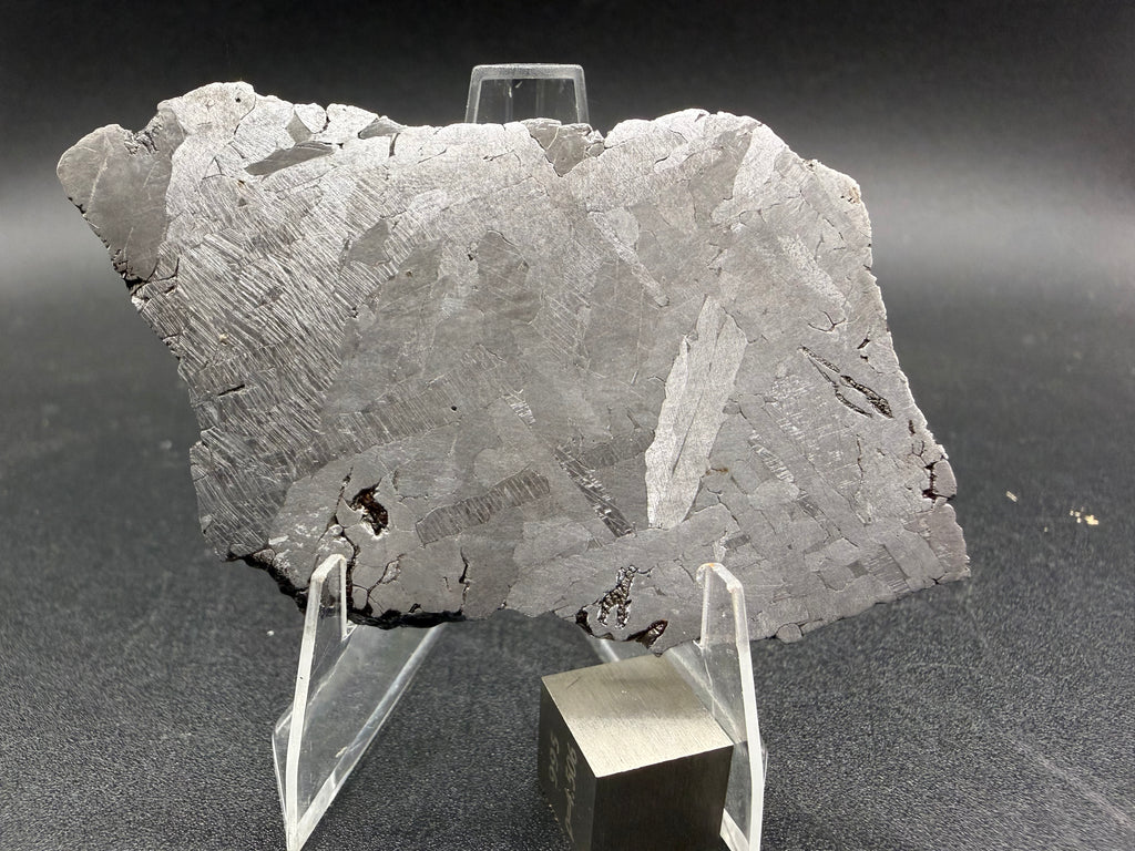 Kaalijarv iron meteorite, IAB-MG, 39.28 g slice standing upright, etched face under bright light with kamacite plates, a bright elongated plate at right, and Neumann bands at left