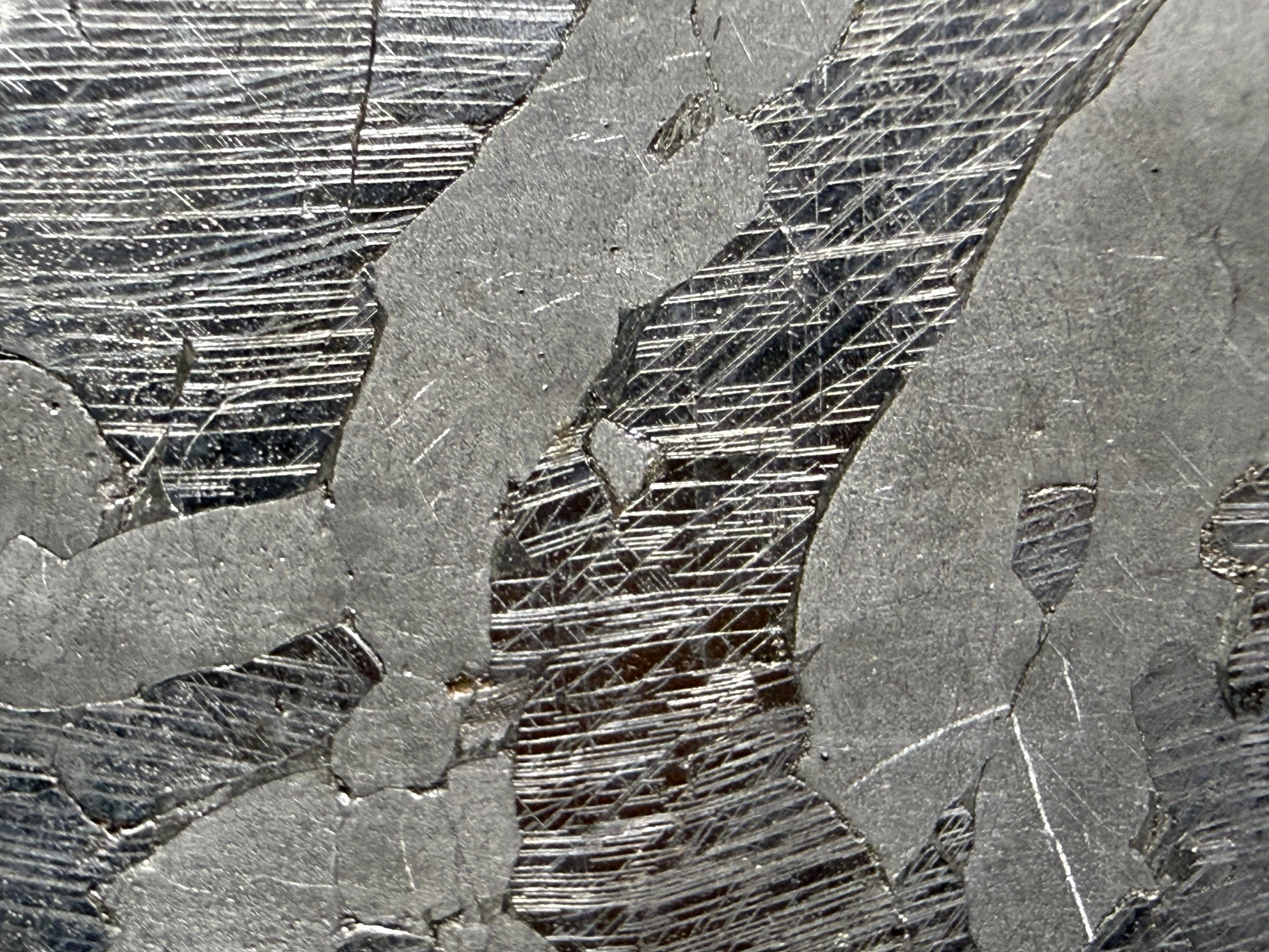 Kaalijarv iron meteorite, IAB-MG, 40.40 g slice, close-up of the etched face showing several intersecting sets of Neumann bands in the darker zones