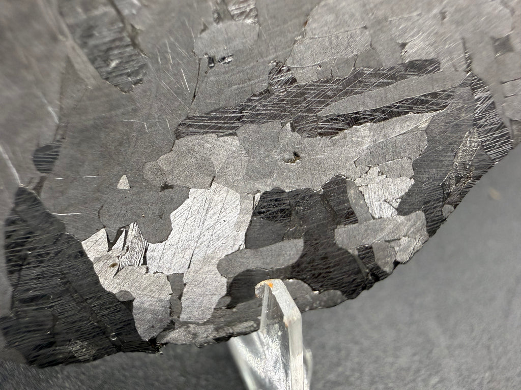 Kaalijarv iron meteorite, IAB-MG, 40.40 g slice, angled close-up of the etched face showing lighter crystal zones and darker zones crossed by sets of Neumann bands
