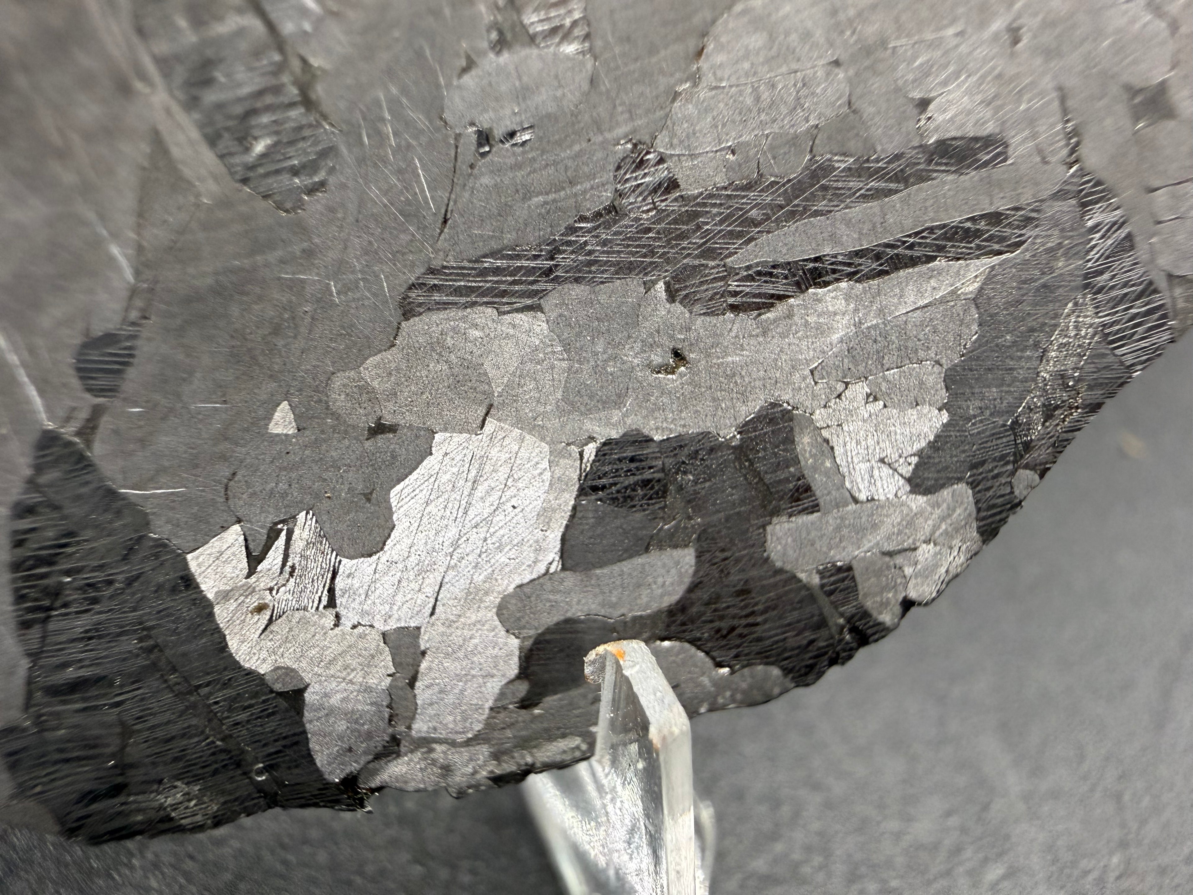 Kaalijarv iron meteorite, IAB-MG, 40.40 g slice, angled close-up of the etched face showing lighter crystal zones and darker zones crossed by sets of Neumann bands