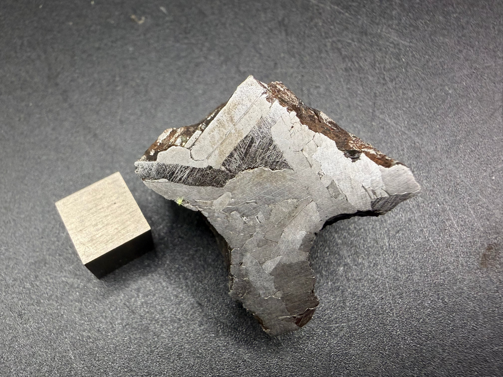 Kaalijarv iron meteorite, IAB-MG, 67.48 g end cut lying flat, etched cut face with lighter crystal zones, darker bands crossed by Neumann bands, and brown weathered exterior along the upper edge