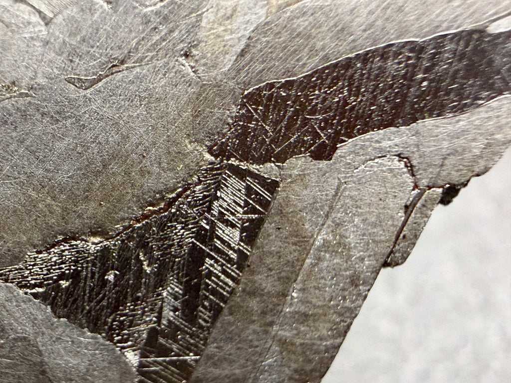 Kaalijarv iron meteorite, IAB-MG, 67.48 g end cut, close-up of the etched face showing fine straight Neumann bands in two darker zones between lighter, smoother metal
