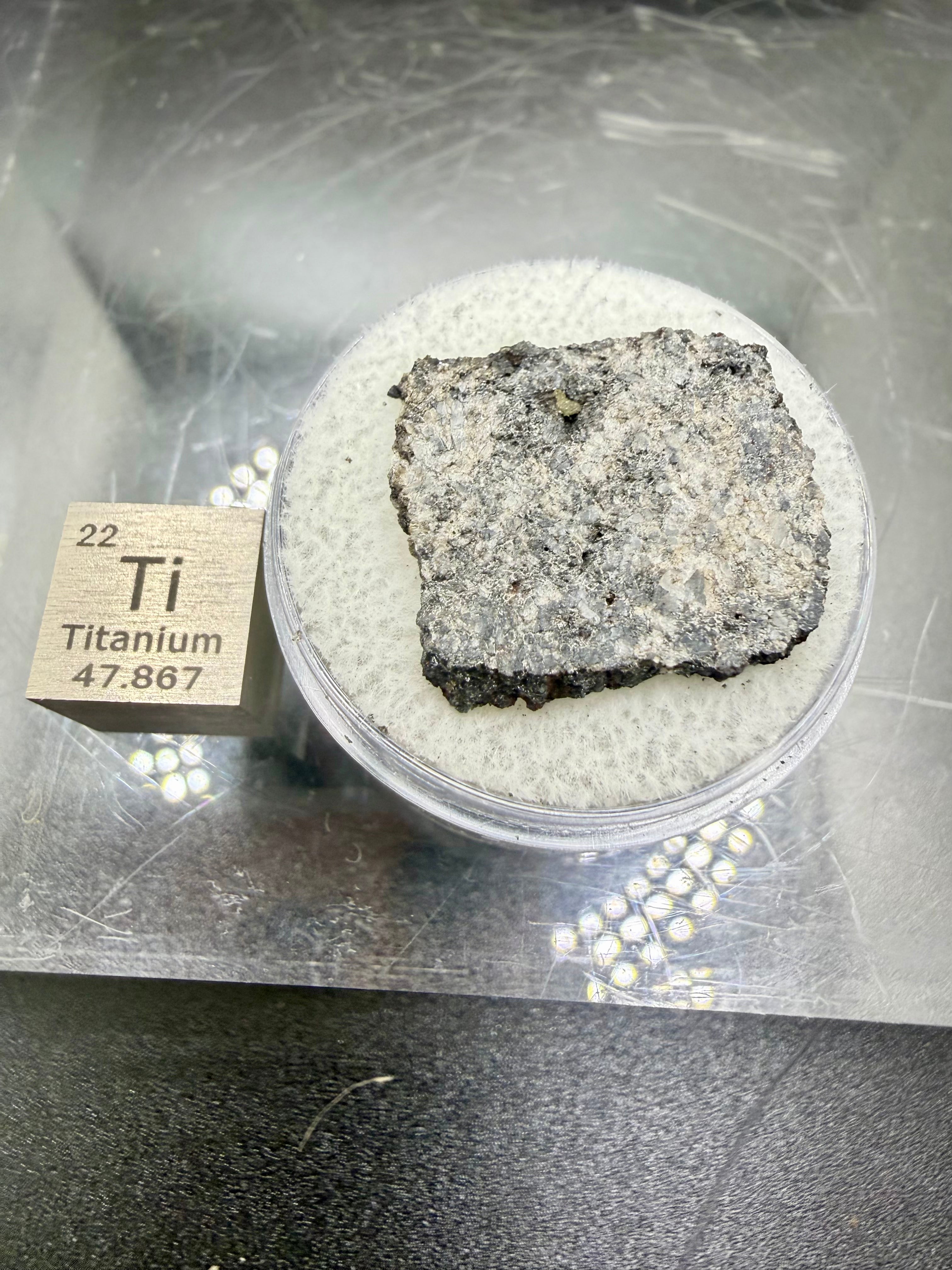 Hero display of Ksar Ghilane 022 ungrouped achondrite meteorite slice in capsule with titanium cube, 2.33g