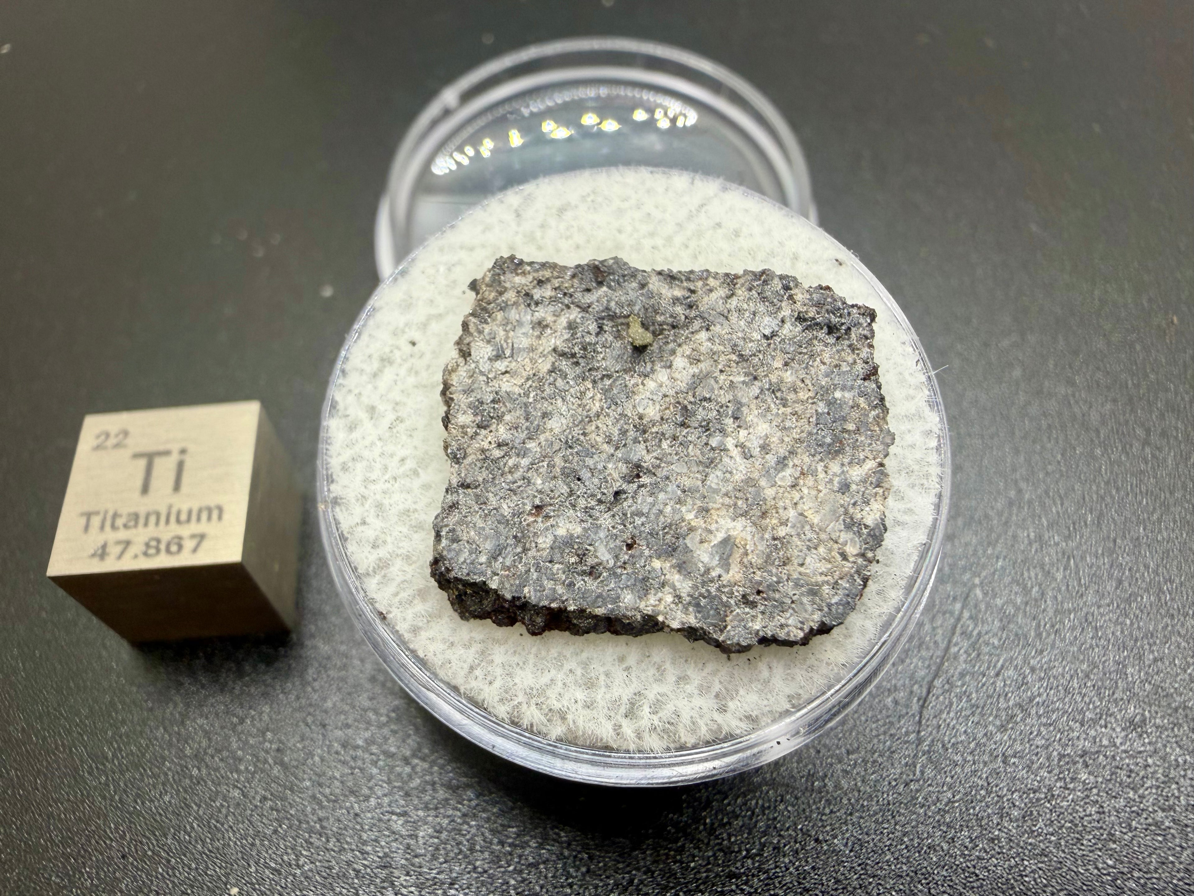 Side view of Ksar Ghilane 022 ungrouped achondrite meteorite slice in capsule with titanium cube reference, 2.33g