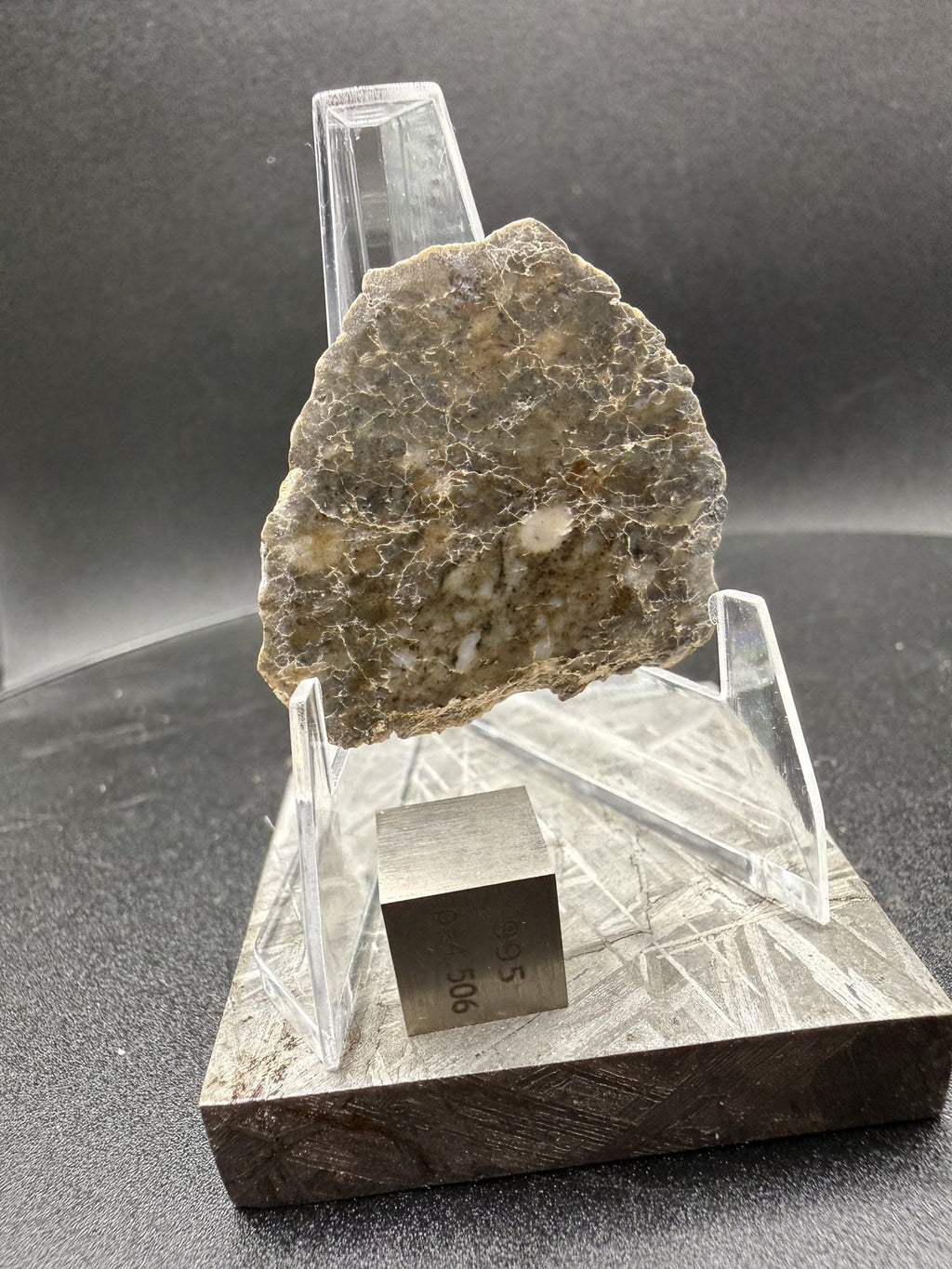 Laayoune 002 lunar meteorite end cut on a display stand with a reference cube for scale, 6.60g