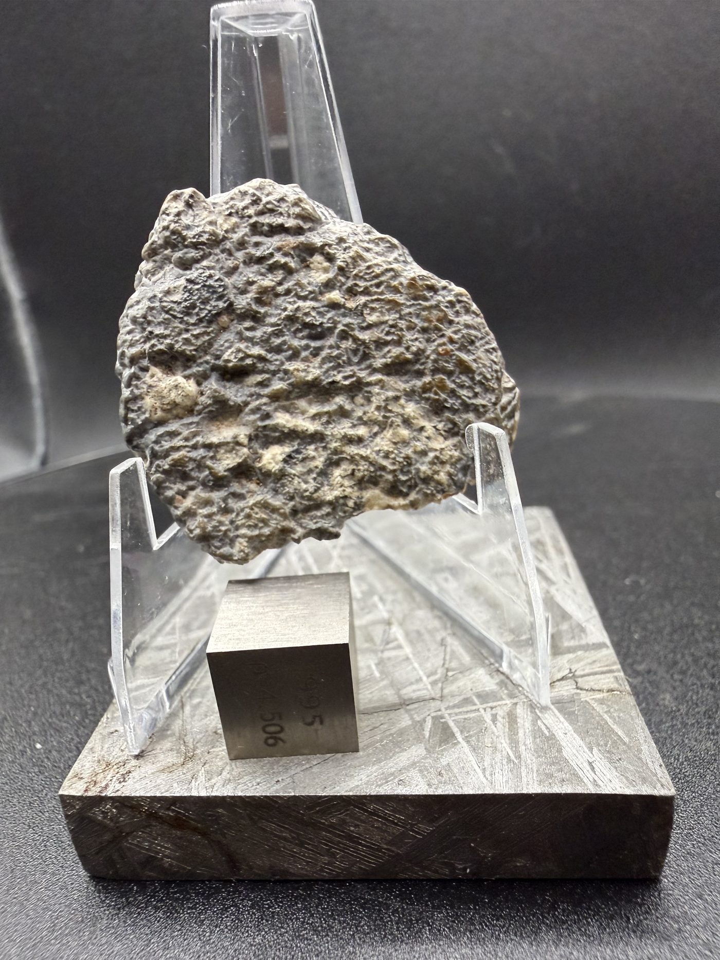 Exterior face of Laayoune 002 lunar meteorite on a display stand with a reference cube for scale, 6.60g