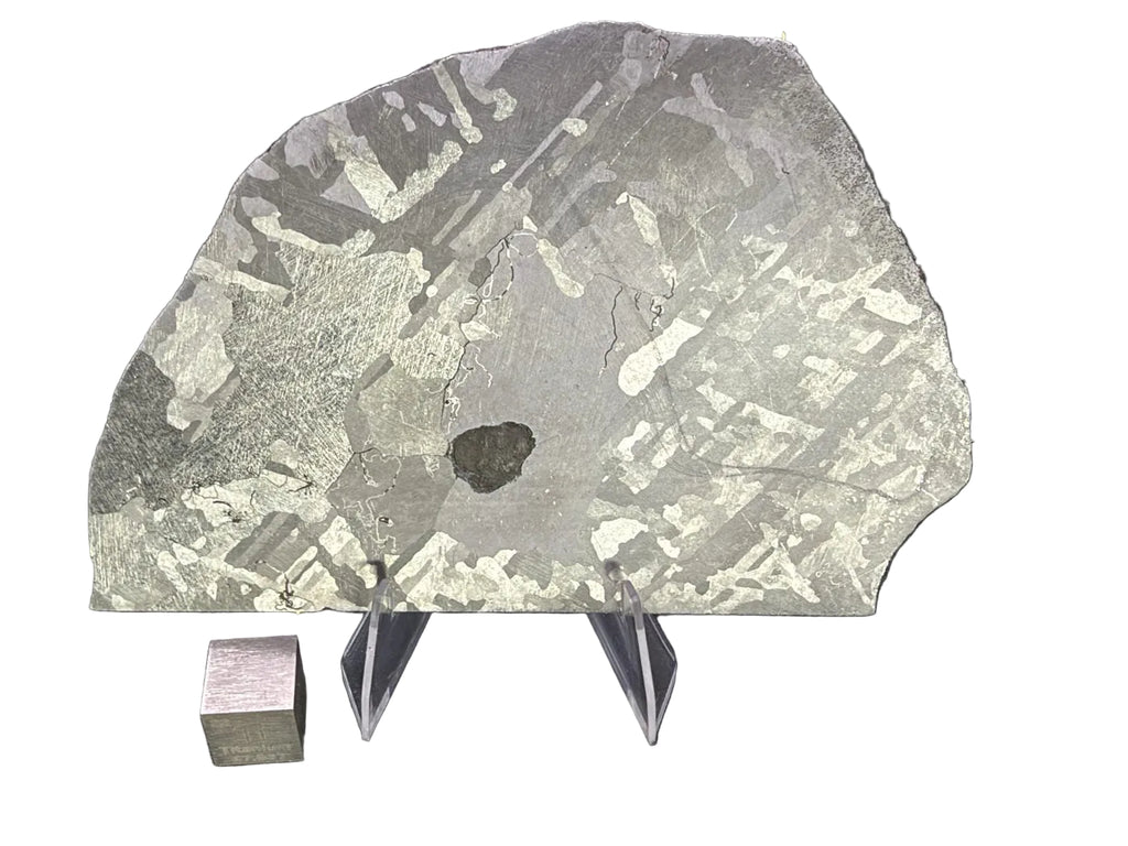 Mount Dooling iron meteorite, IC, 105.76 g slice on a clear acrylic stand with a scale cube against a dark background, polished and etched face showing crossing kamacite plates, large metal grains and a dark central inclusion