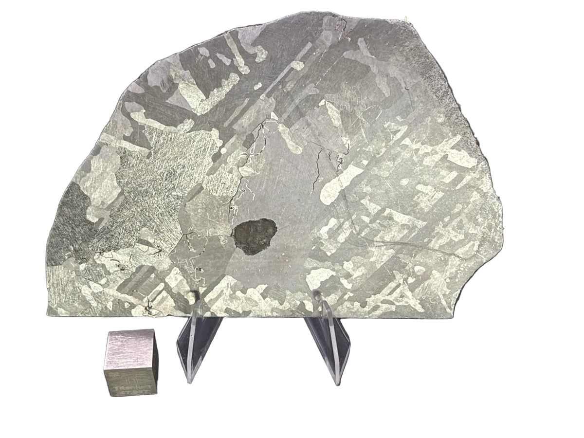 Mount Dooling iron meteorite, IC, 105.76 g slice on a clear acrylic stand with a scale cube against a dark background, polished and etched face showing crossing kamacite plates, large metal grains and a dark central inclusion
