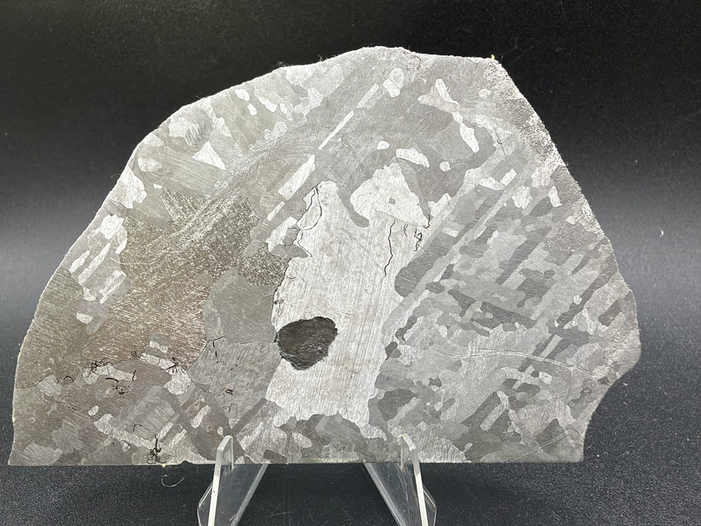 Mount Dooling iron meteorite, IC, 105.76 g slice on a clear acrylic stand, polished and etched face showing bright kamacite plates, differently oriented gray grains and a dark central inclusion