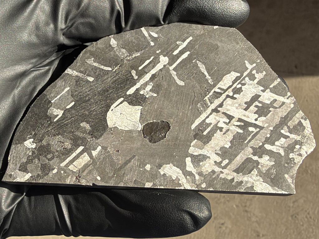 Mount Dooling iron meteorite, IC, 105.76 g slice in daylight, polished and etched face angled to light the bright kamacite plates crossing the dark gray grains