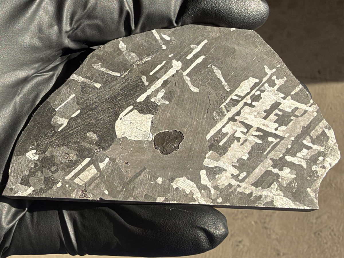 Mount Dooling iron meteorite, IC, 105.76 g slice in daylight, polished and etched face angled to light the bright kamacite plates crossing the dark gray grains