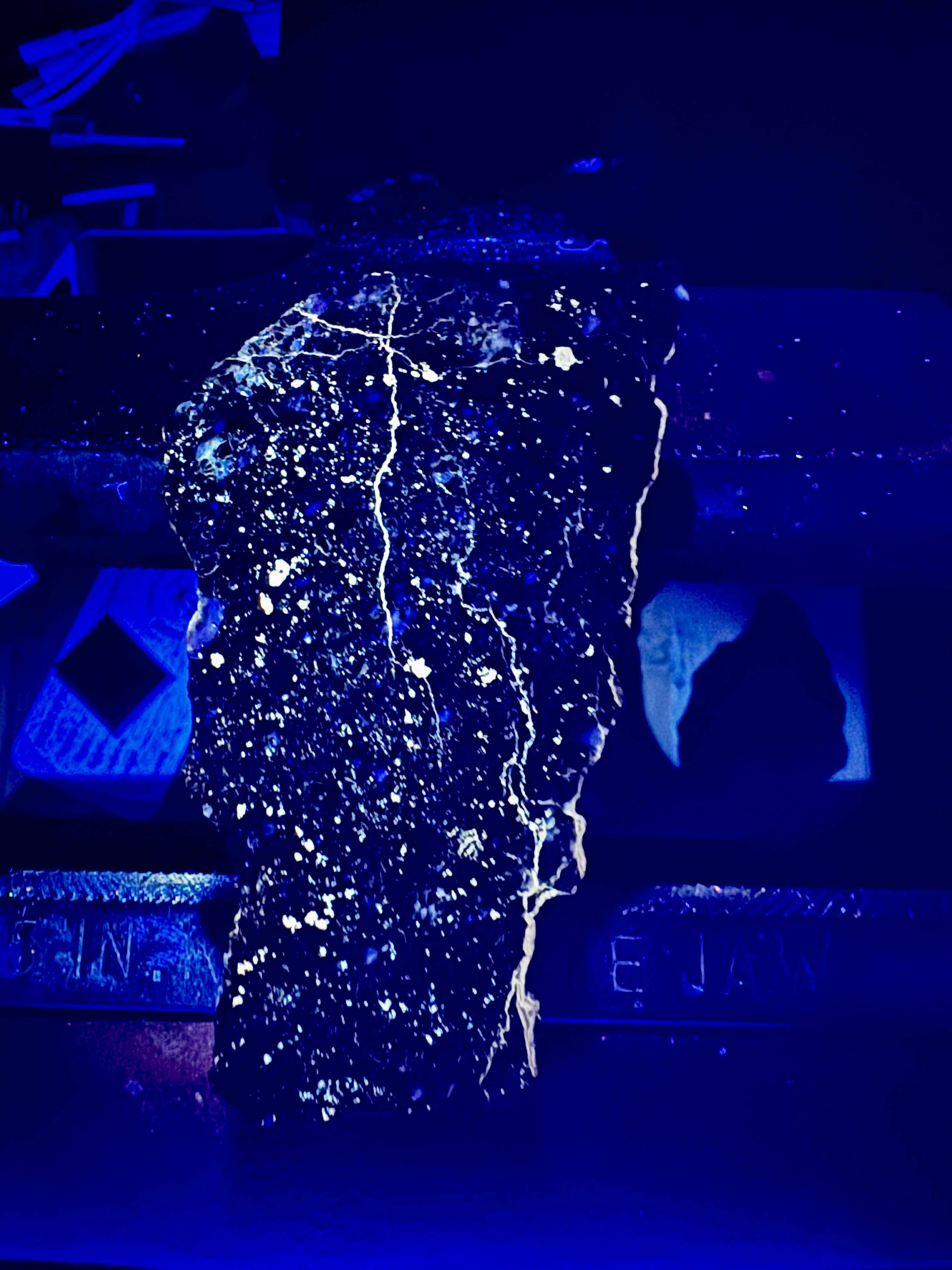 NWA 18452 eucrite breccia meteorite slice showing fluorescence and phosphorescence under UV light