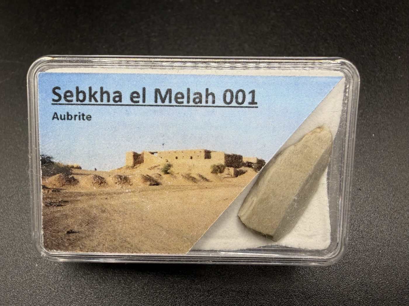 Sebkha el Melah 001 aubrite, 2.51g individual enstatite crystal beside labeled display box