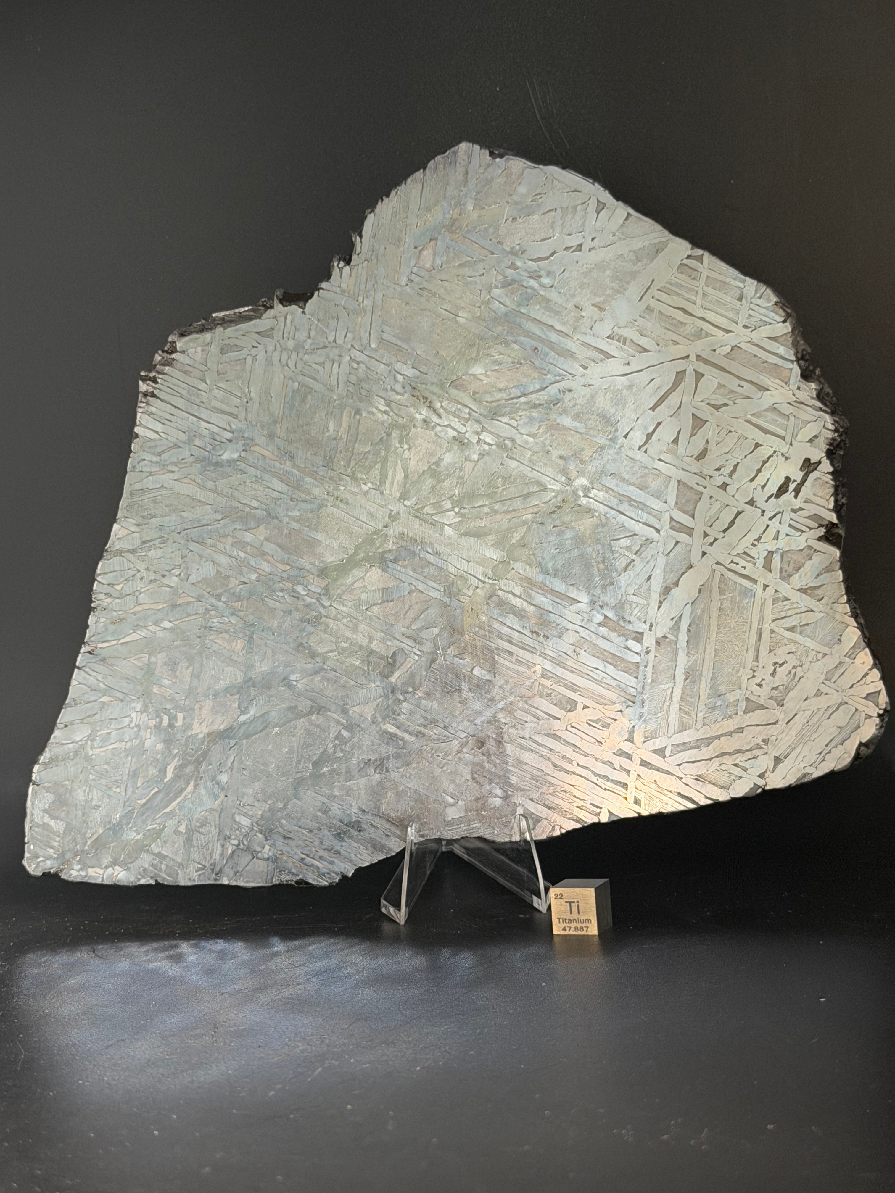 Seymchan pallasite 591g full slice on acrylic display stand with titanium element cube for scale